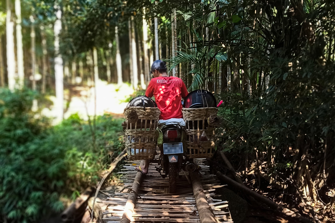 A humanitarian worker crosses a bridge on a motorcycle while traveling to deliver assistance to conflict-affected communities in Karen (Kayin) State, Myanmar. 
