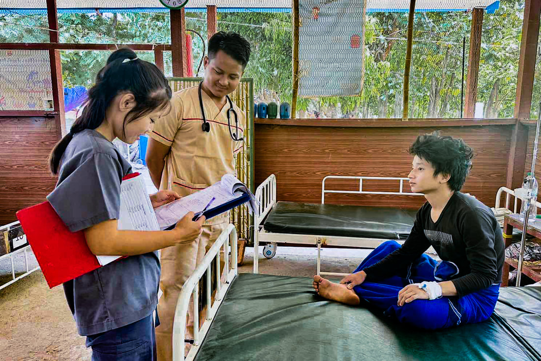 YSDA clinic-in-charge Saw Moo Kler and a colleague consult notes at the bedside of a patient at a clinic in Bago Region, Myanmar.