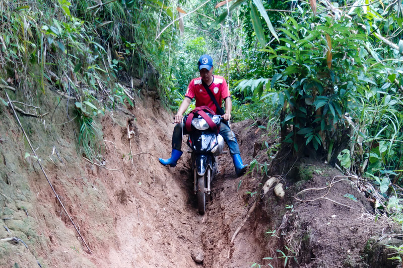 A humanitarian worker navigates a narrow and muddy path by motorcycle in Karen (Kayin) State, Myanmar. 