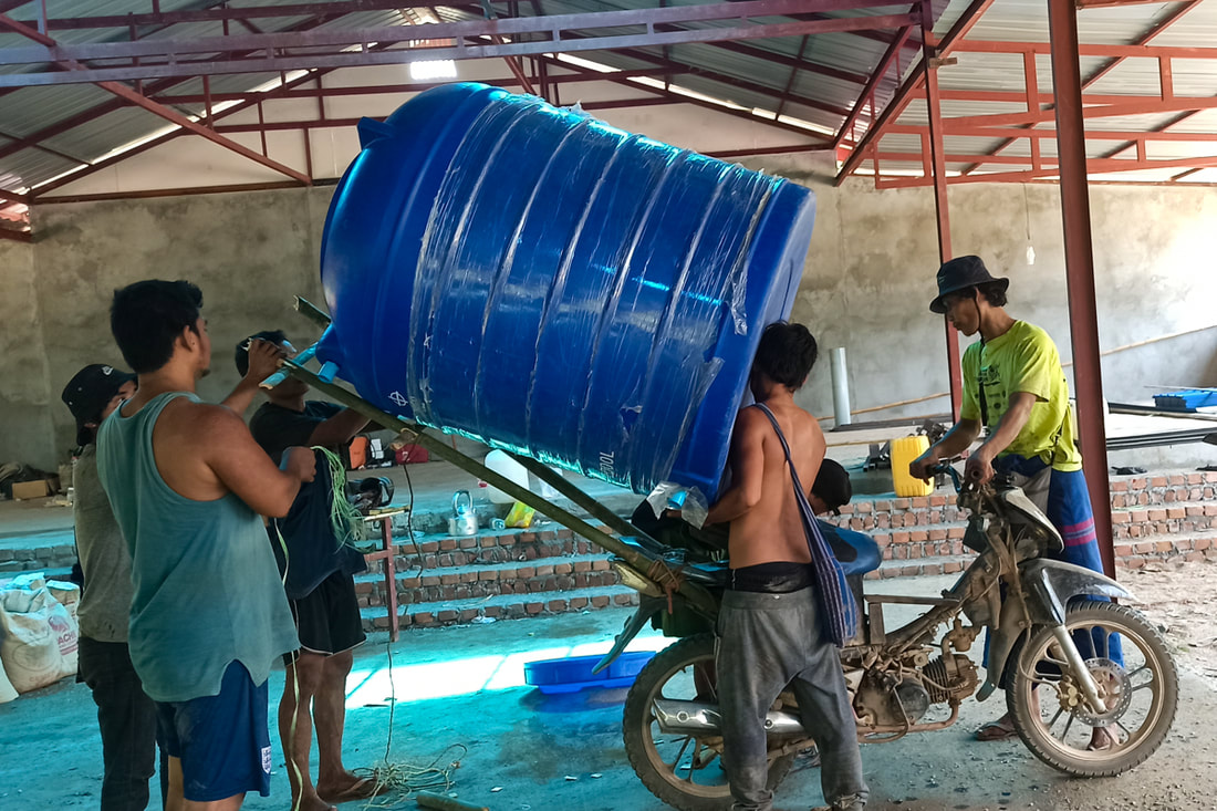 Humanitarian workers in Karen (Kayin) State, Myanmar, secure a water tank to the back of a motorcycle.