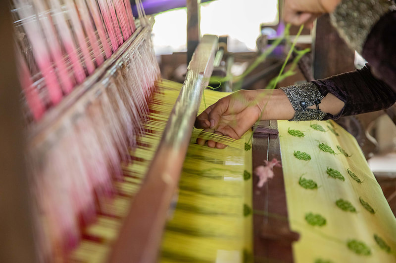 A weaver adjusts the thread on her loom. 