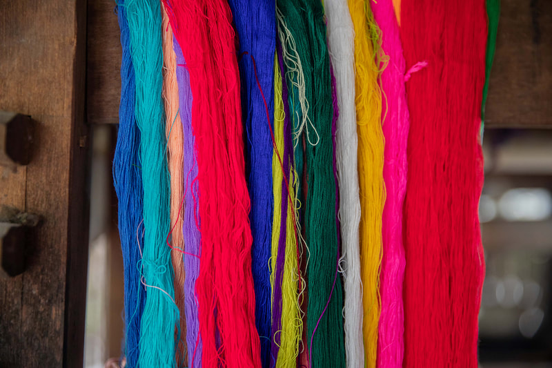 Multicolored yarns hang from a loom.
