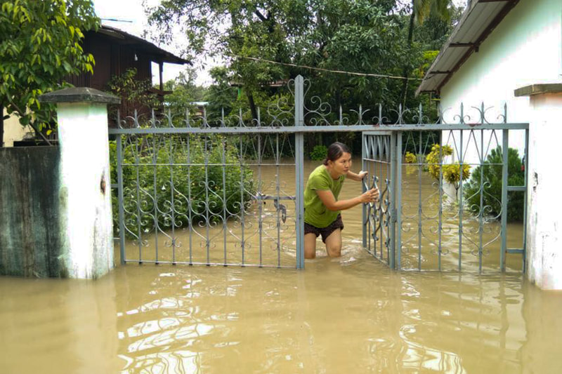 A woman stands at the gate of a flooded property in Karen (Kayin) State, Myanmar. 
