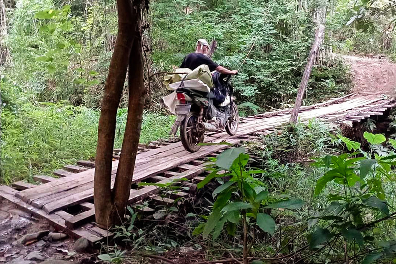 A humanitarian worker pushes a motorcycle across a wooden bridge in Karen (Kayin) State, Myanmar.